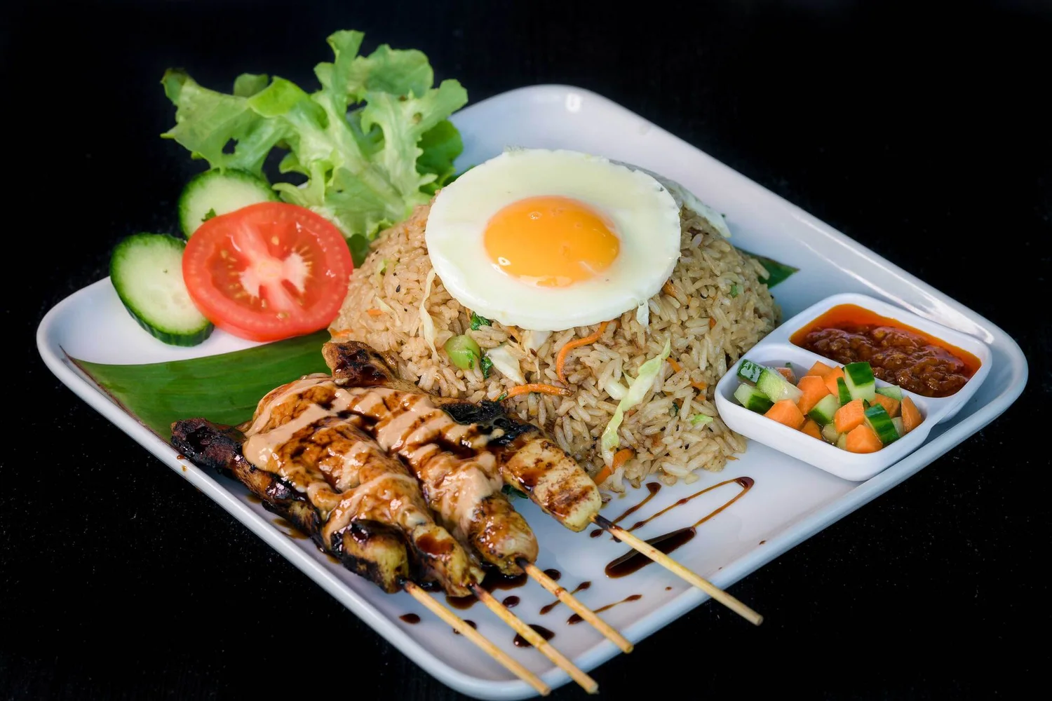 Bagus Cafe fried rice topped with a fried egg, served with four chicken satay skewers, salad and sauces